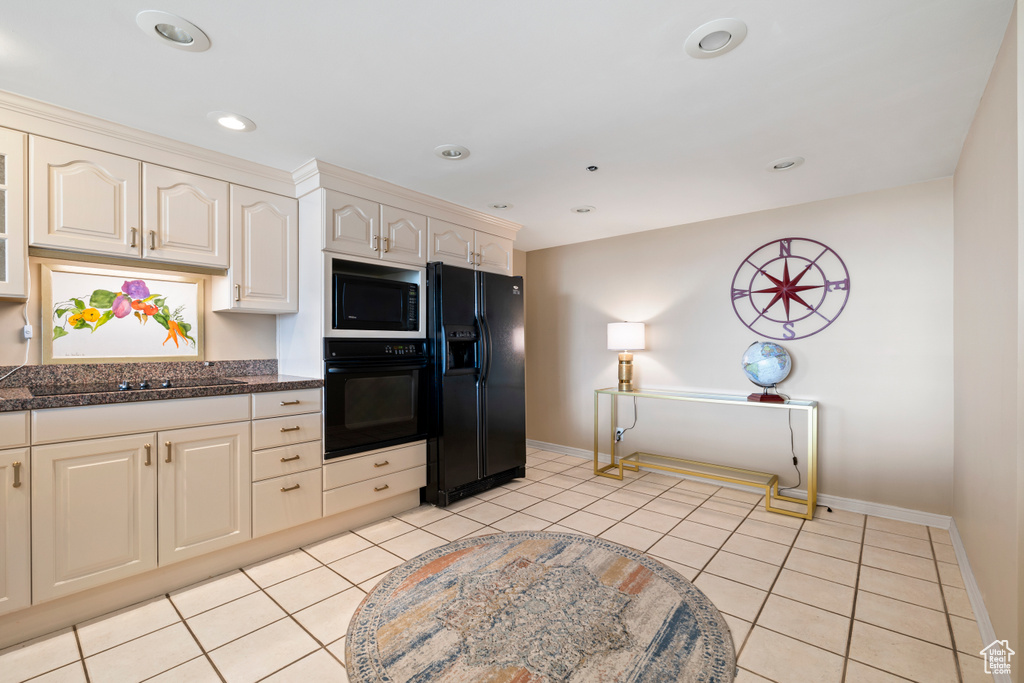 Kitchen featuring light tile flooring, dark stone counters, and black appliances