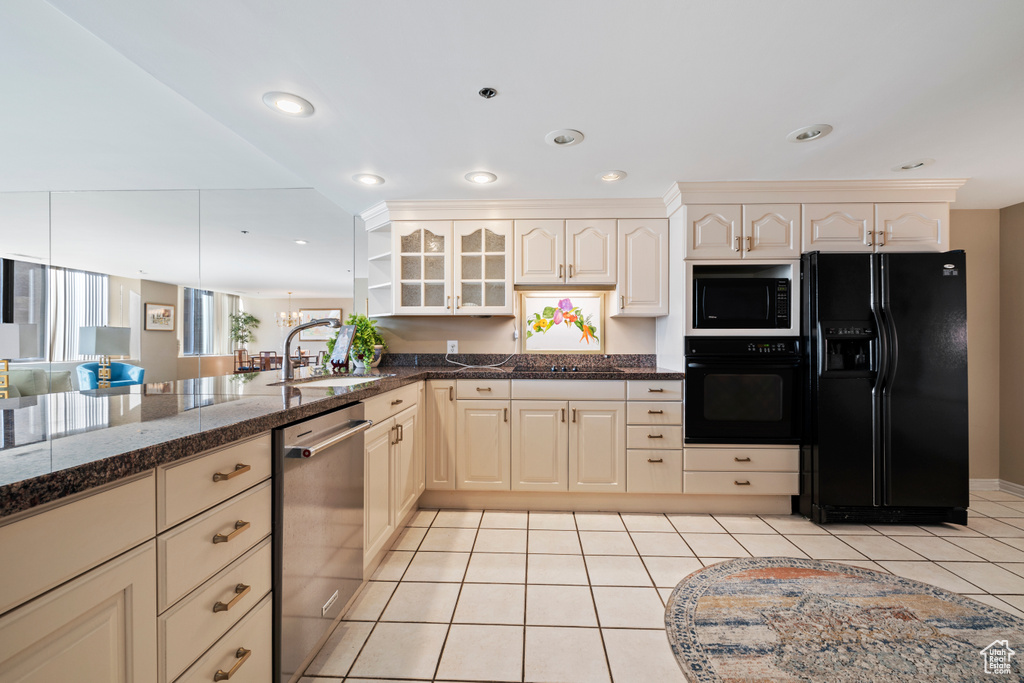 Kitchen with kitchen peninsula, black appliances, dark stone countertops, light tile floors, and sink