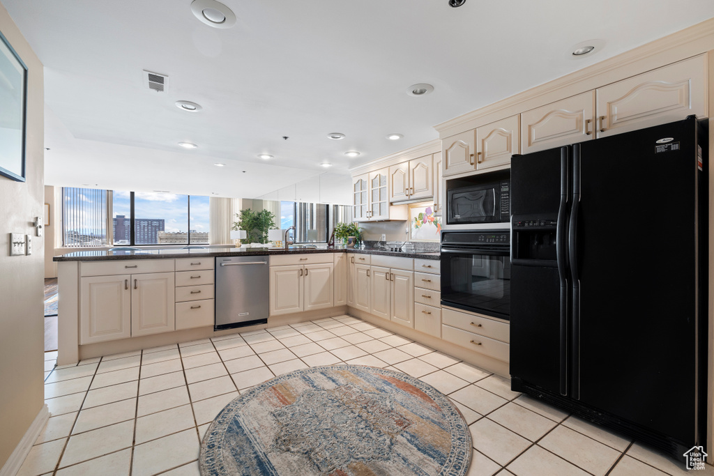 Kitchen with black appliances, cream cabinetry, light tile flooring, and kitchen peninsula
