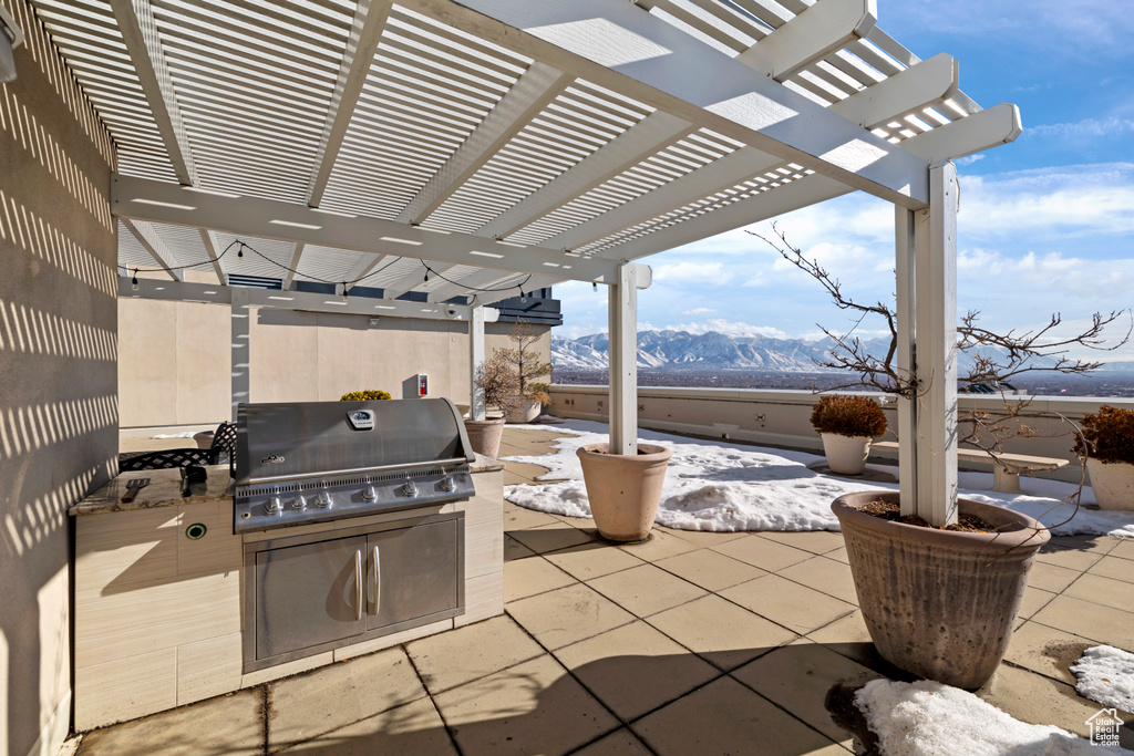Snow covered patio with a grill, a pergola, a mountain view, and an outdoor kitchen