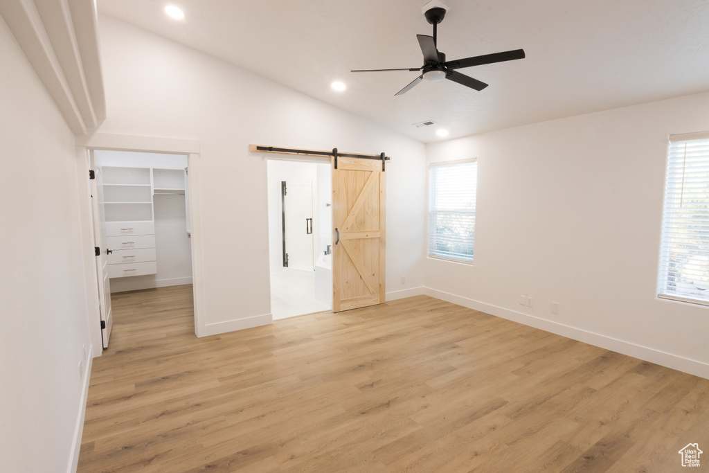 Unfurnished bedroom with a barn door, light hardwood / wood-style floors, ceiling fan, a walk in closet, and lofted ceiling