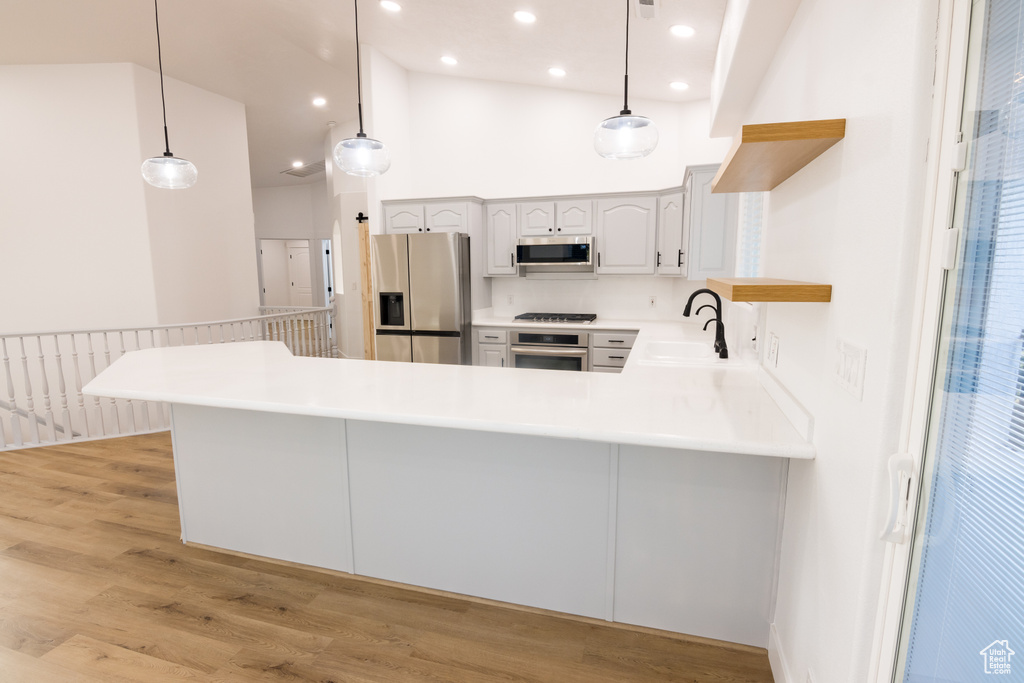 Kitchen featuring hanging light fixtures, white cabinets, appliances with stainless steel finishes, light hardwood / wood-style flooring, and high vaulted ceiling