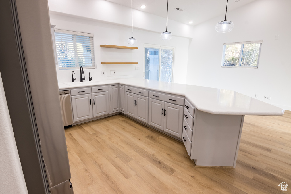 Kitchen featuring sink, dishwasher, light wood-type flooring, and pendant lighting