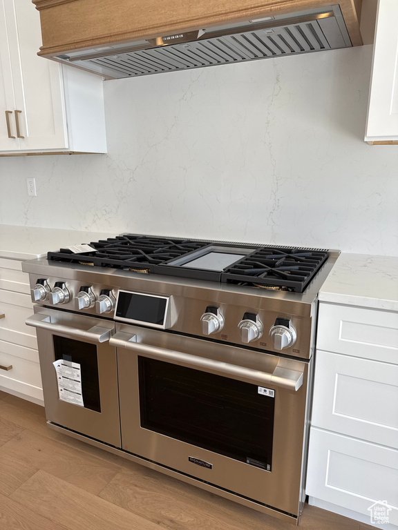Kitchen featuring ventilation hood, double oven range, tasteful backsplash, and white cabinets