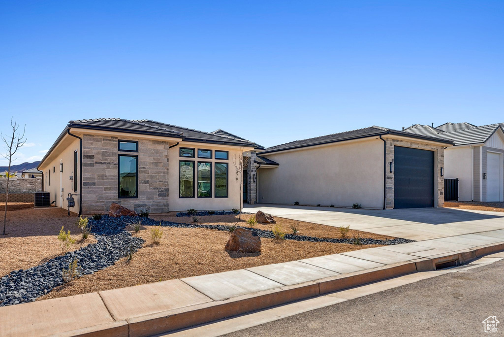 View of front of home featuring an attached garage, central AC, stone siding, stucco siding, and concrete driveway