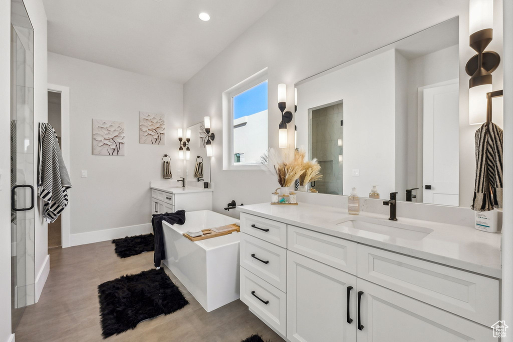 Full bath featuring a freestanding bath, a sink, two vanities, a shower stall, and wood finished floors