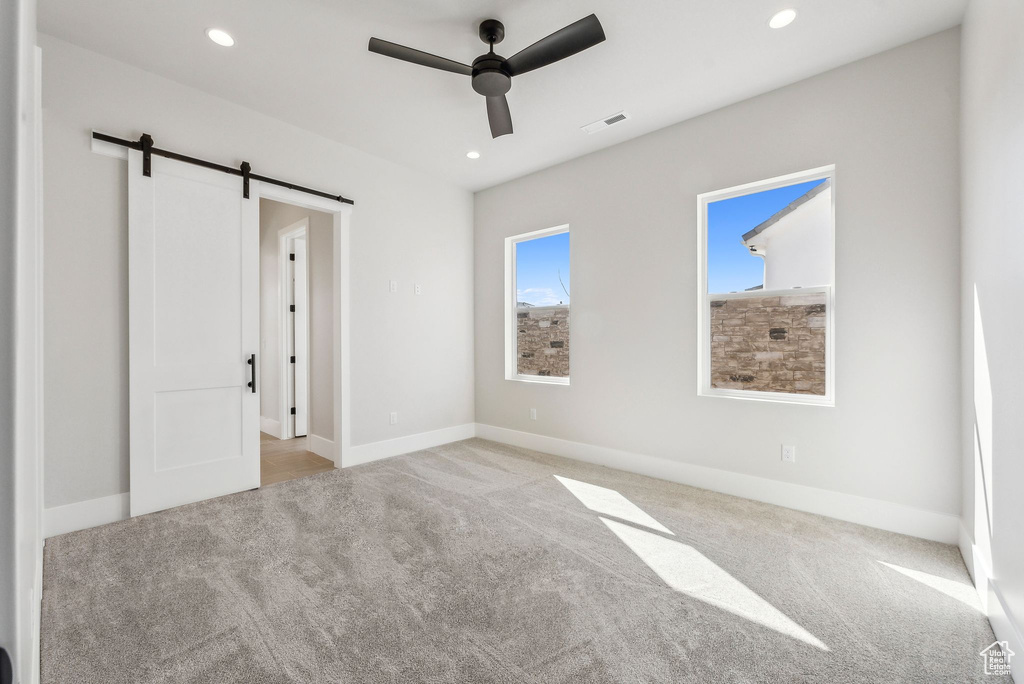 Unfurnished bedroom with carpet flooring, recessed lighting, visible vents, and a barn door