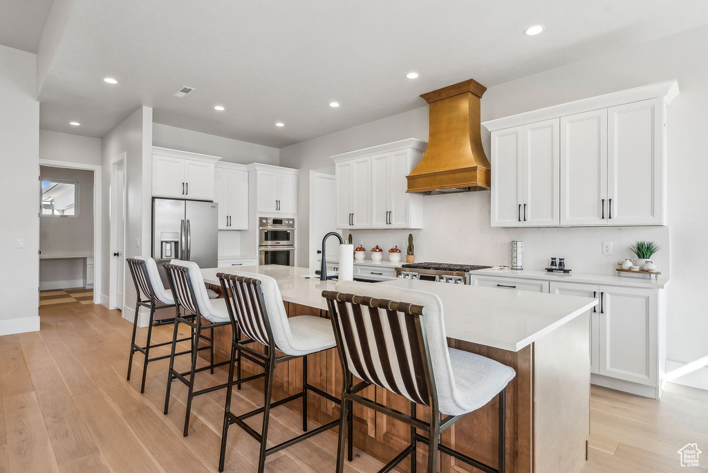 Kitchen with light wood-style flooring, premium range hood, stainless steel appliances, a large island, and recessed lighting