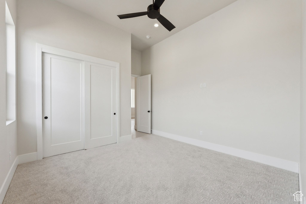 Unfurnished bedroom featuring a closet, baseboards, ceiling fan, light colored carpet, and vaulted ceiling