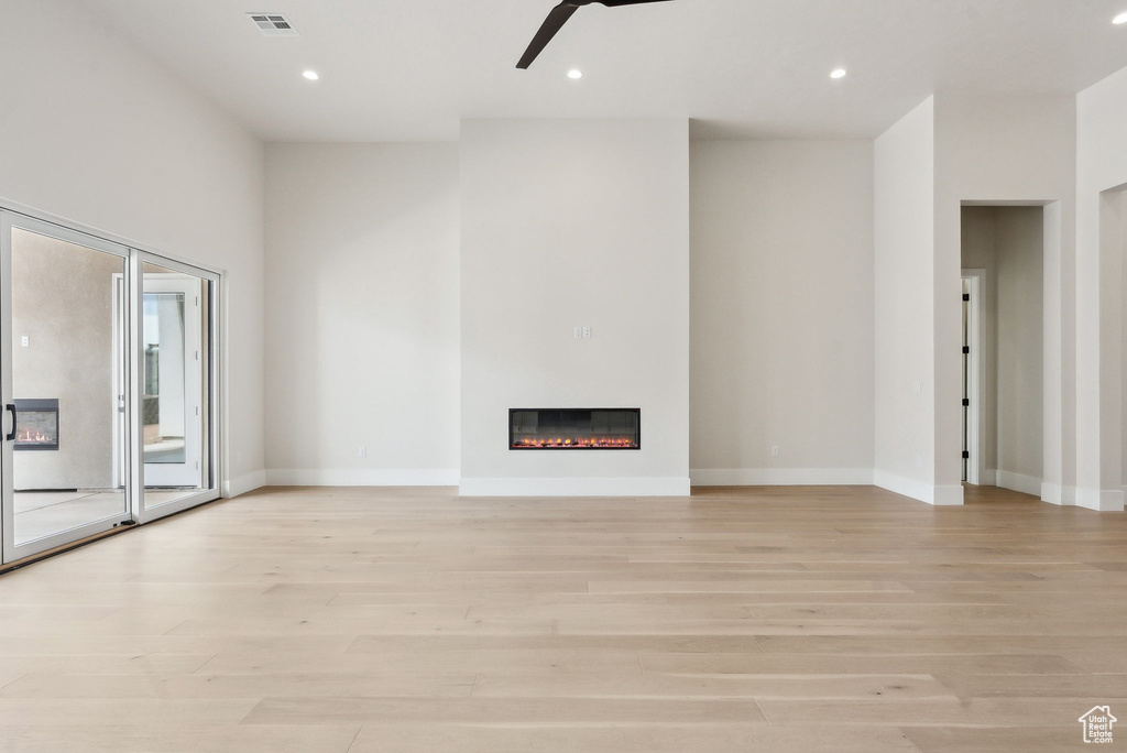 Unfurnished living room with visible vents, light wood-style floors, ceiling fan, and a glass covered fireplace