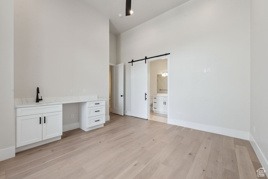 Unfurnished bedroom with a towering ceiling, a barn door, a sink, light wood finished floors, and ensuite bathroom