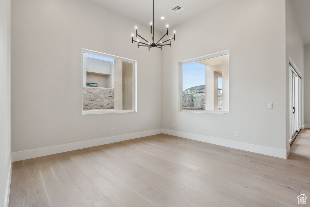 Empty room with baseboards, a notable chandelier, light wood-style flooring, and visible vents