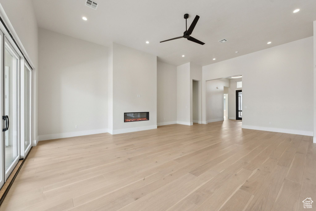 Unfurnished living room featuring a ceiling fan, visible vents, light wood-type flooring, a glass covered fireplace, and recessed lighting