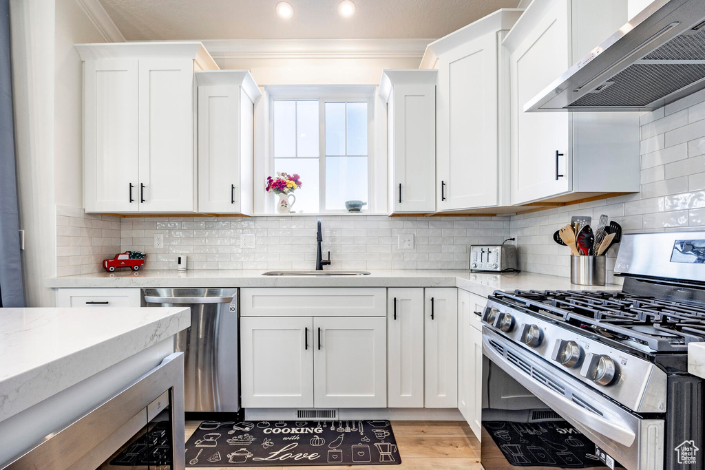 Kitchen featuring wall chimney exhaust hood, tasteful backsplash, appliances with stainless steel finishes, and white cabinets