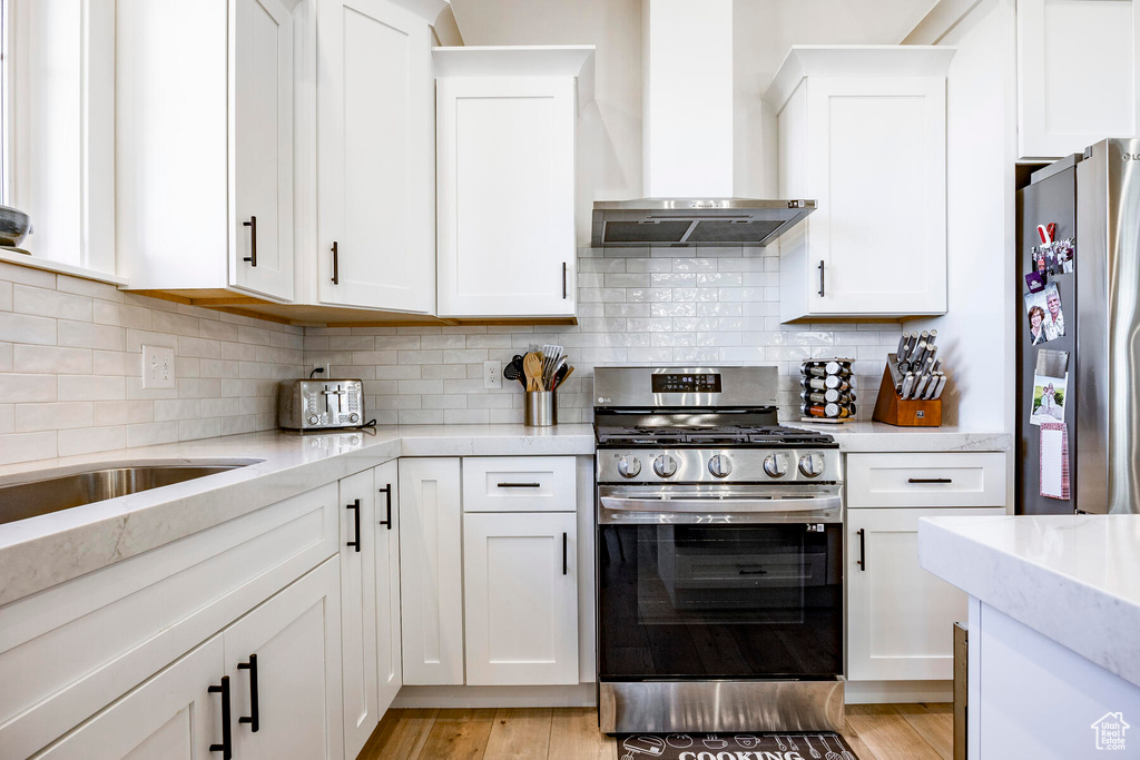 Kitchen featuring wall chimney exhaust hood, white cabinets, and appliances with stainless steel finishes