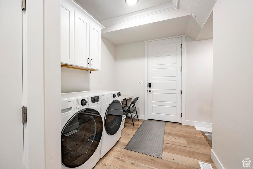 Clothes washing area with light hardwood / wood-style floors, washer and clothes dryer, and cabinets