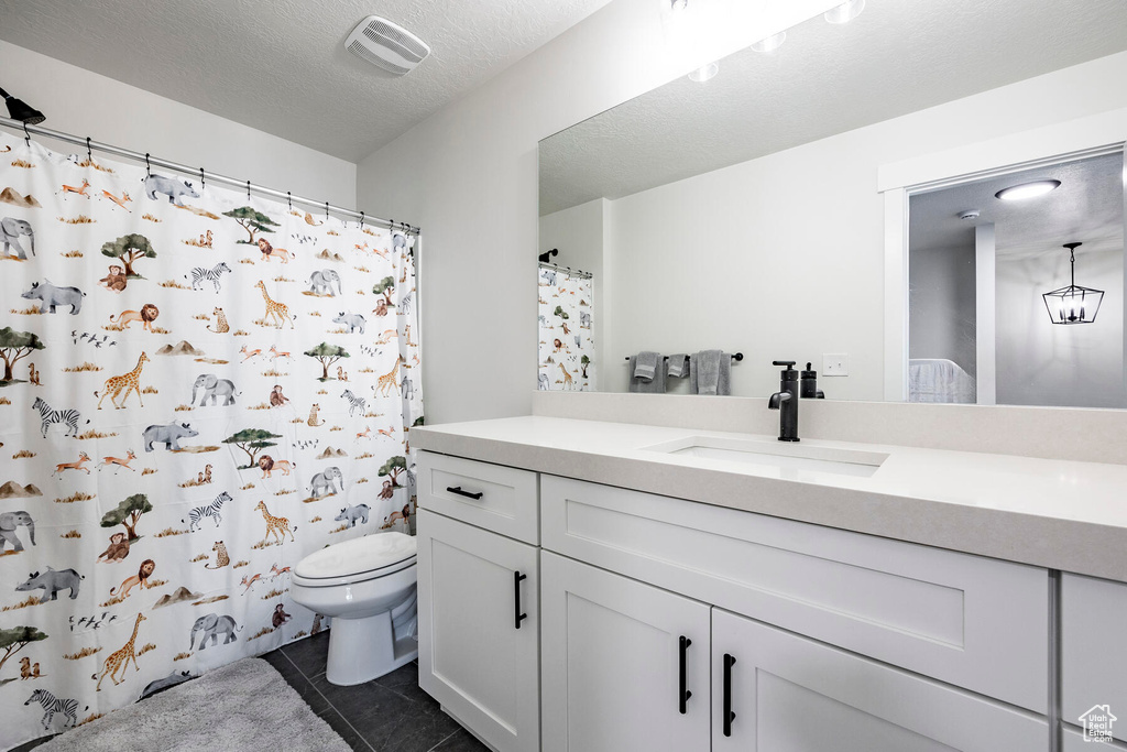 Bathroom with tile floors, toilet, vanity, and a textured ceiling