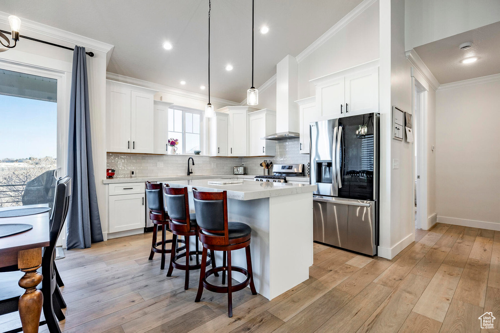 Kitchen featuring light hardwood / wood-style floors, a kitchen island, appliances with stainless steel finishes, decorative light fixtures, and white cabinets