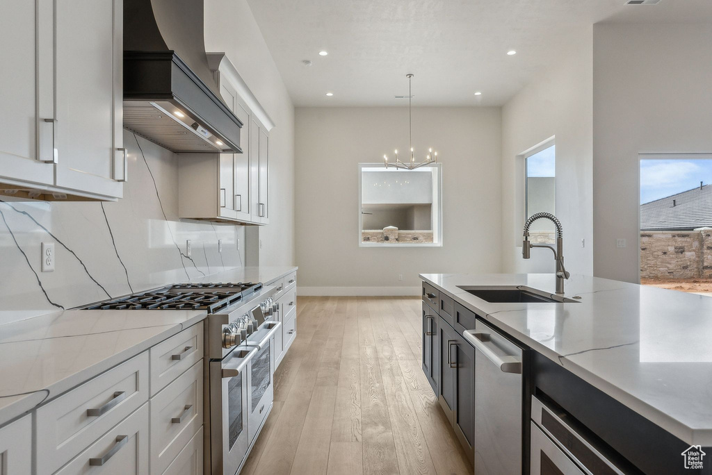 Kitchen featuring appliances with stainless steel finishes, a sink, light wood-style flooring, premium range hood, and decorative light fixtures