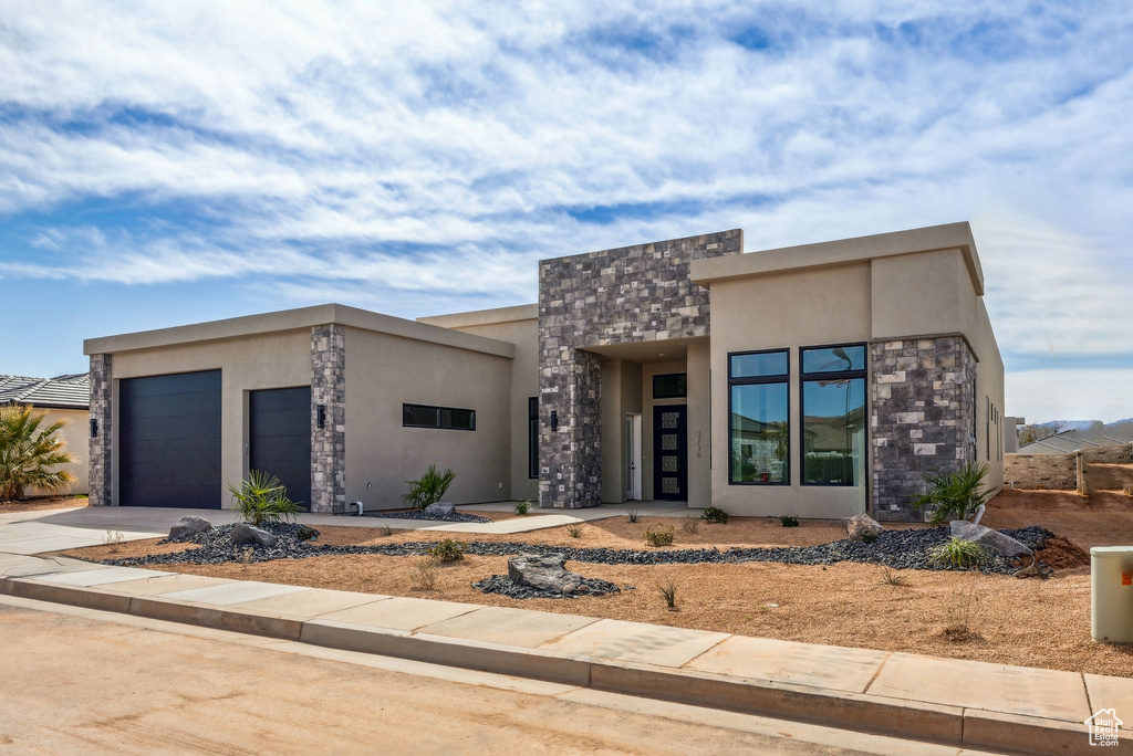 View of front of house featuring an attached garage, driveway, stone siding, and stucco siding