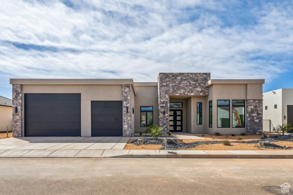 Contemporary house featuring an attached garage, stucco siding, stone siding, and concrete driveway