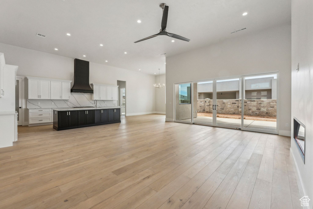 Unfurnished living room featuring recessed lighting, a towering ceiling, ceiling fan with notable chandelier, and light wood-type flooring