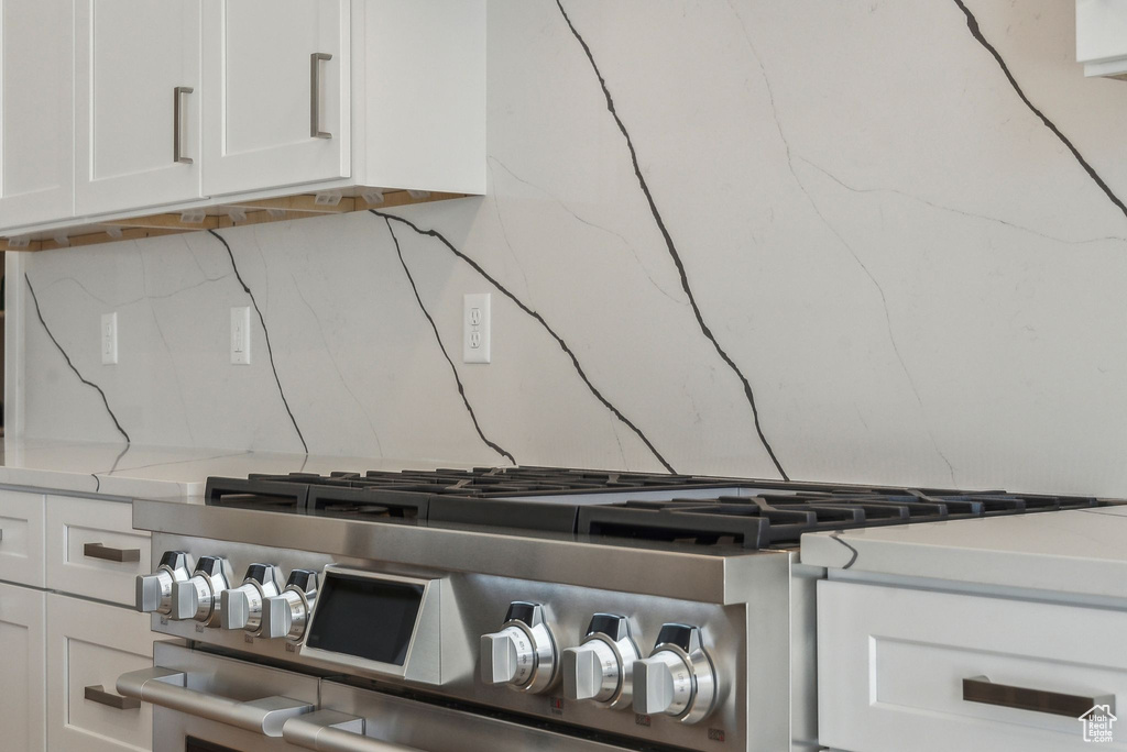 Room details with decorative backsplash, stainless steel range, white cabinets, and light stone countertops