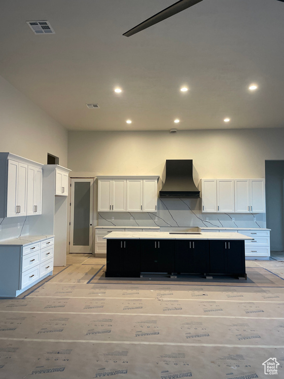Kitchen with a spacious island, premium range hood, white cabinetry, light wood-type flooring, and decorative backsplash