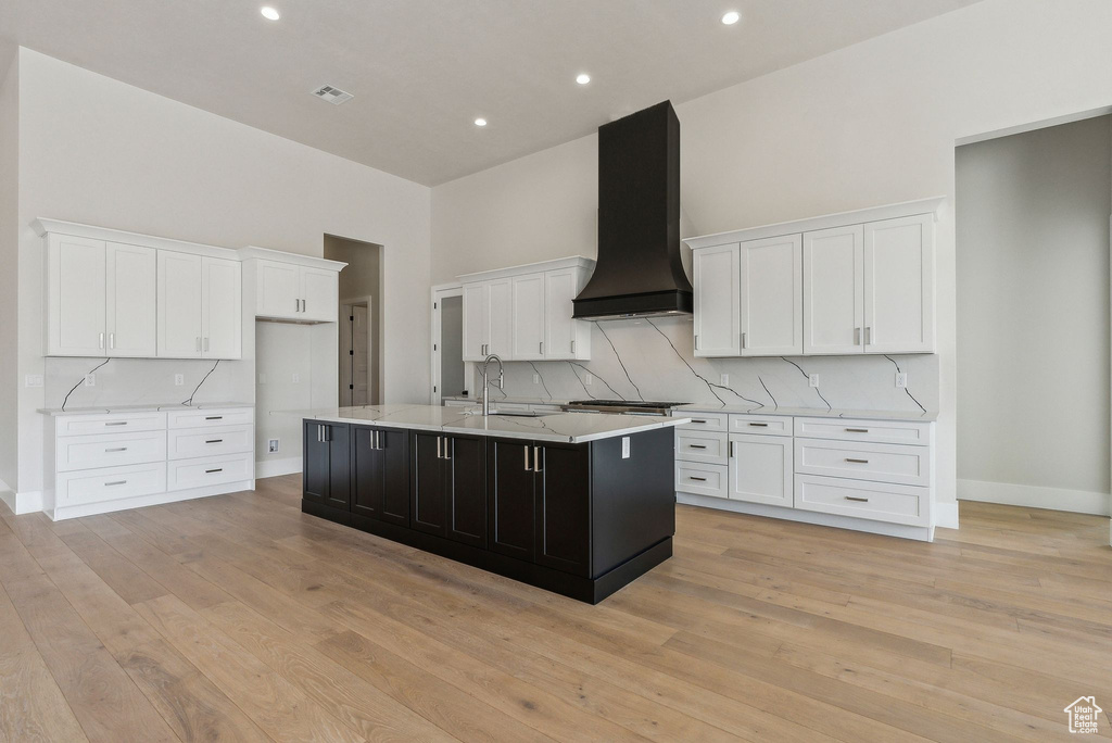 Kitchen with a sink, white cabinetry, an island with sink, and exhaust hood