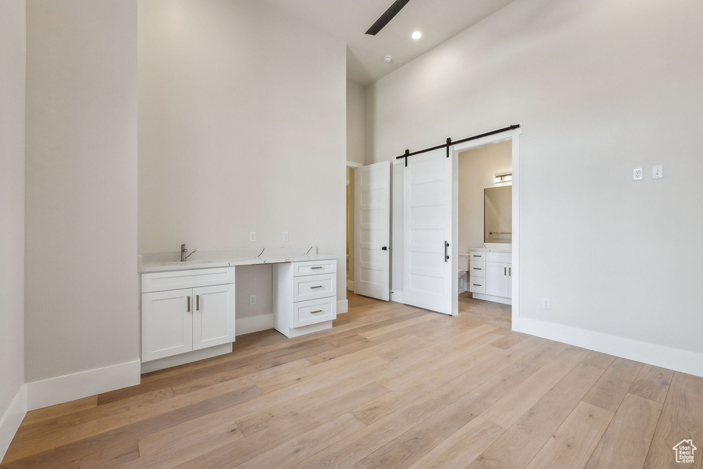 Unfurnished bedroom featuring a towering ceiling, baseboards, light wood-type flooring, a barn door, and a sink
