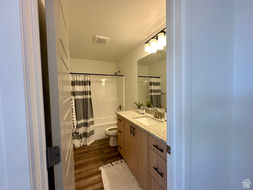 Full bathroom featuring vanity with extensive cabinet space, a textured ceiling, shower / bath combo, hardwood / wood-style flooring, and toilet