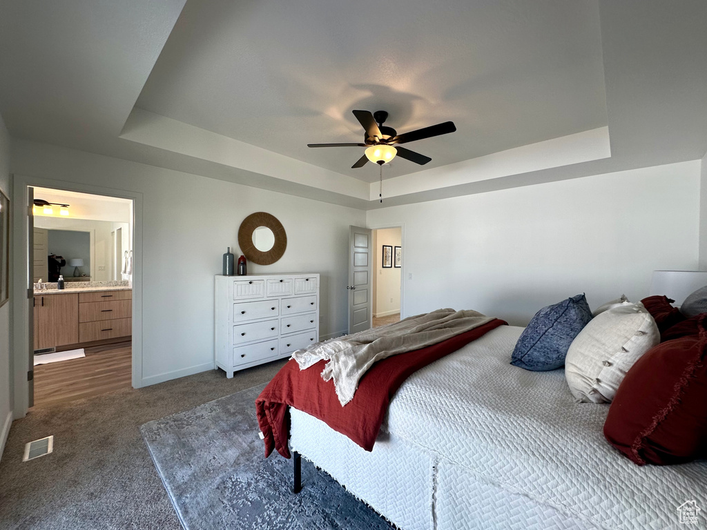 Bedroom with carpet flooring, ensuite bathroom, ceiling fan, and a raised ceiling