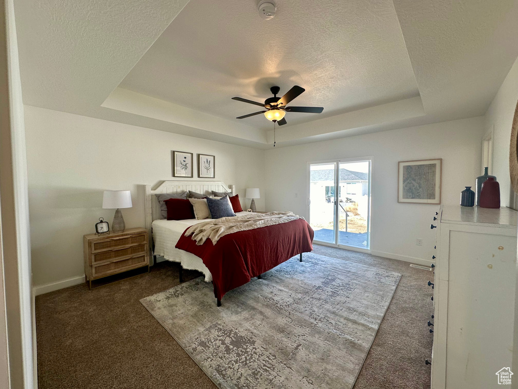 Carpeted bedroom featuring a raised ceiling, a textured ceiling, access to outside, and ceiling fan