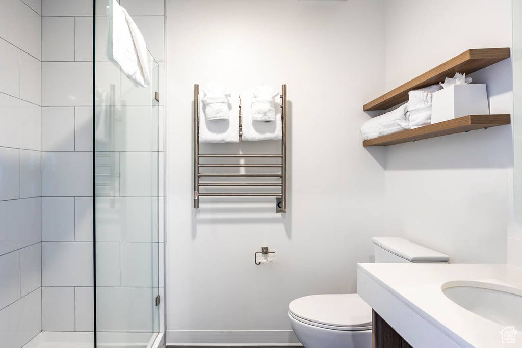 Bathroom featuring a shower with shower door, toilet, vanity, and radiator heating unit