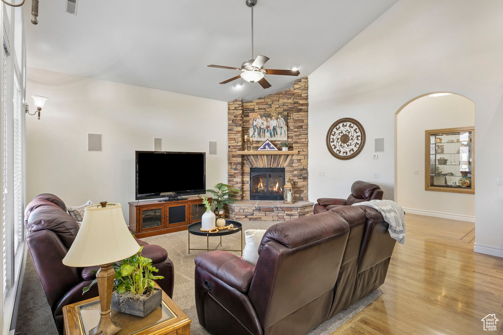 Living room with a stone fireplace, light wood-type flooring, high vaulted ceiling, and ceiling fan