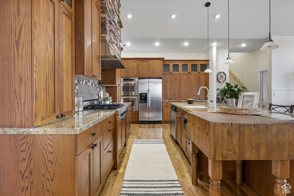 Kitchen featuring appliances with stainless steel finishes, pendant lighting, backsplash, sink, and light wood-type flooring