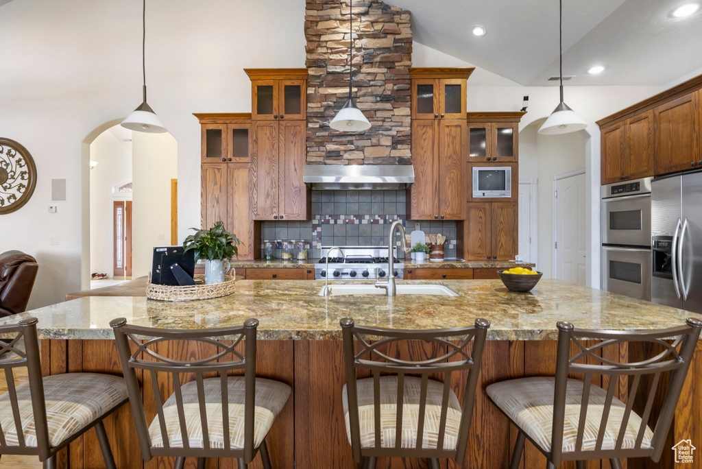Kitchen featuring a kitchen bar, appliances with stainless steel finishes, decorative light fixtures, and backsplash