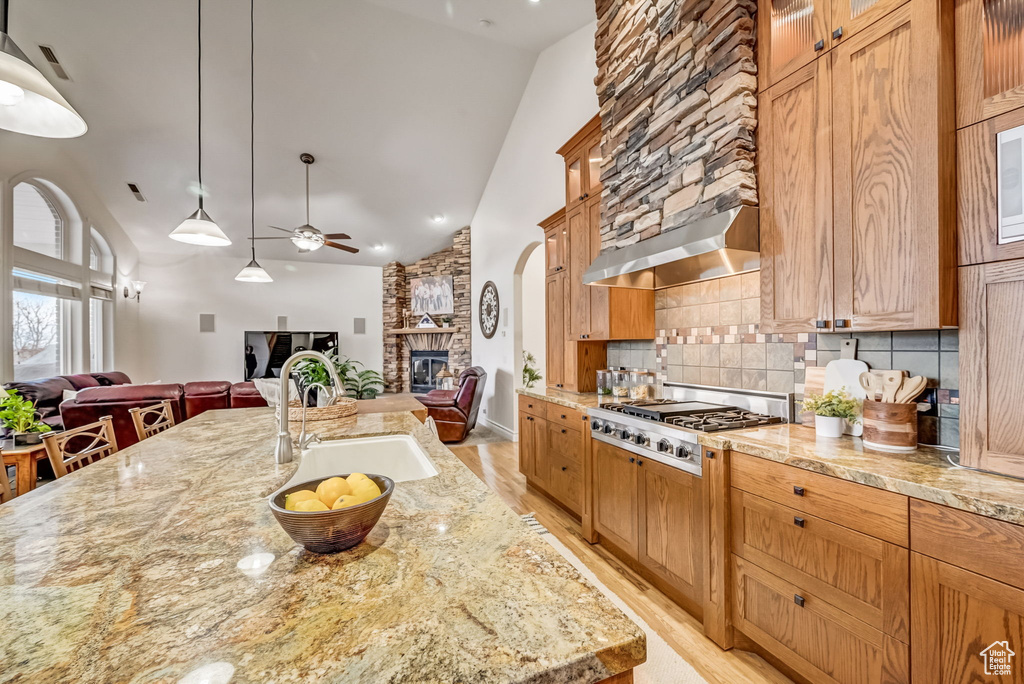 Kitchen featuring light hardwood / wood-style floors, ceiling fan, tasteful backsplash, sink, and a stone fireplace