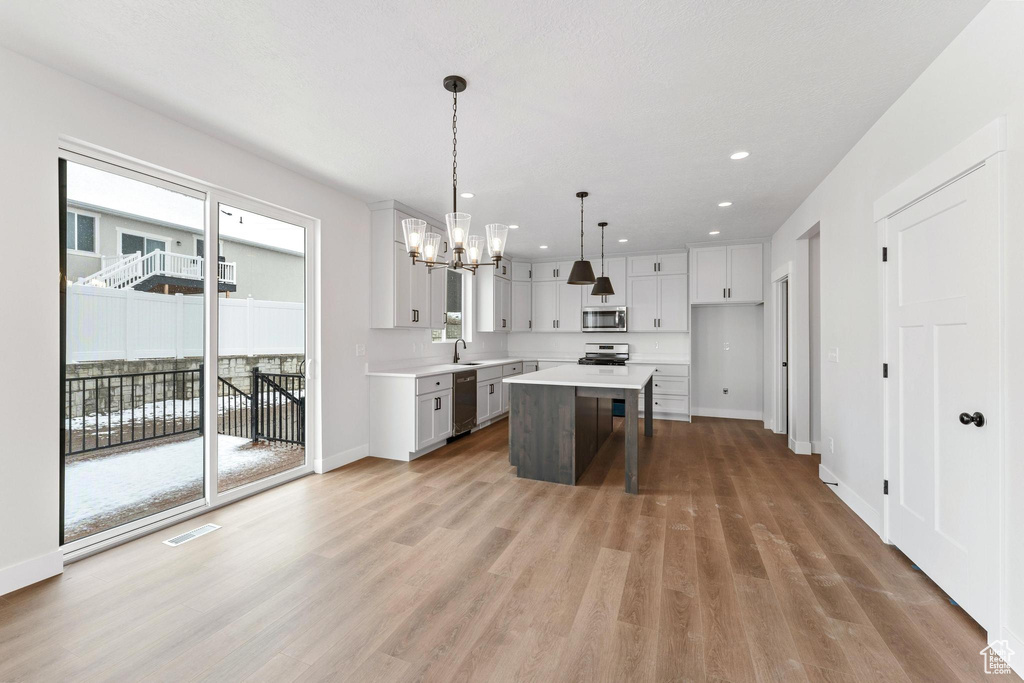 Kitchen featuring light hardwood / wood-style flooring, white cabinets, hanging light fixtures, a center island, and appliances with stainless steel finishes