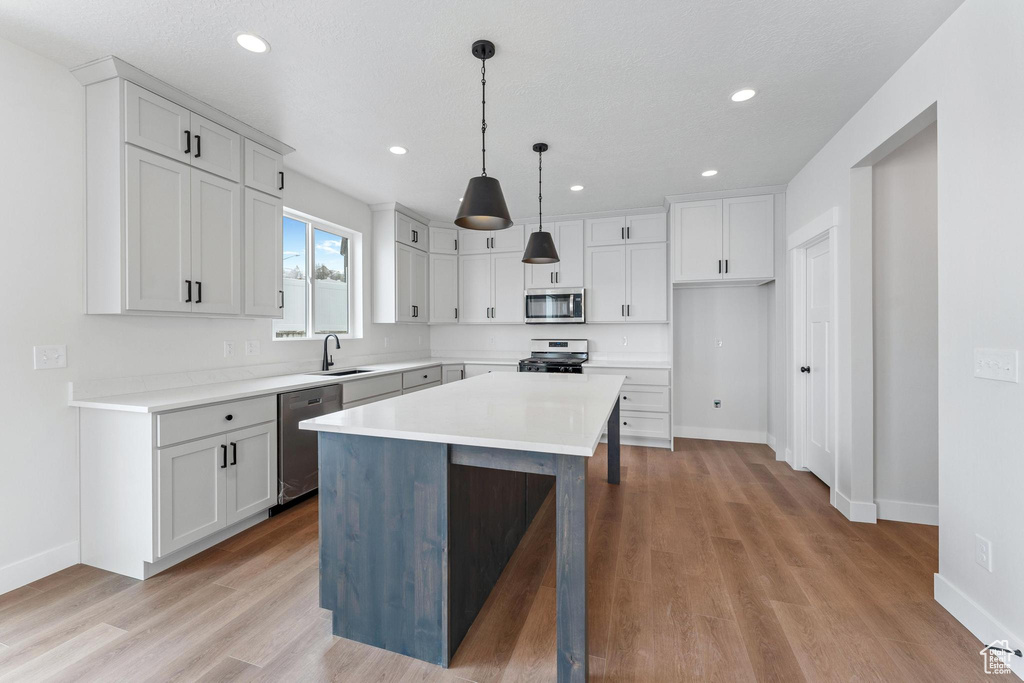 Kitchen featuring stainless steel appliances, a kitchen island, light hardwood / wood-style flooring, sink, and decorative light fixtures