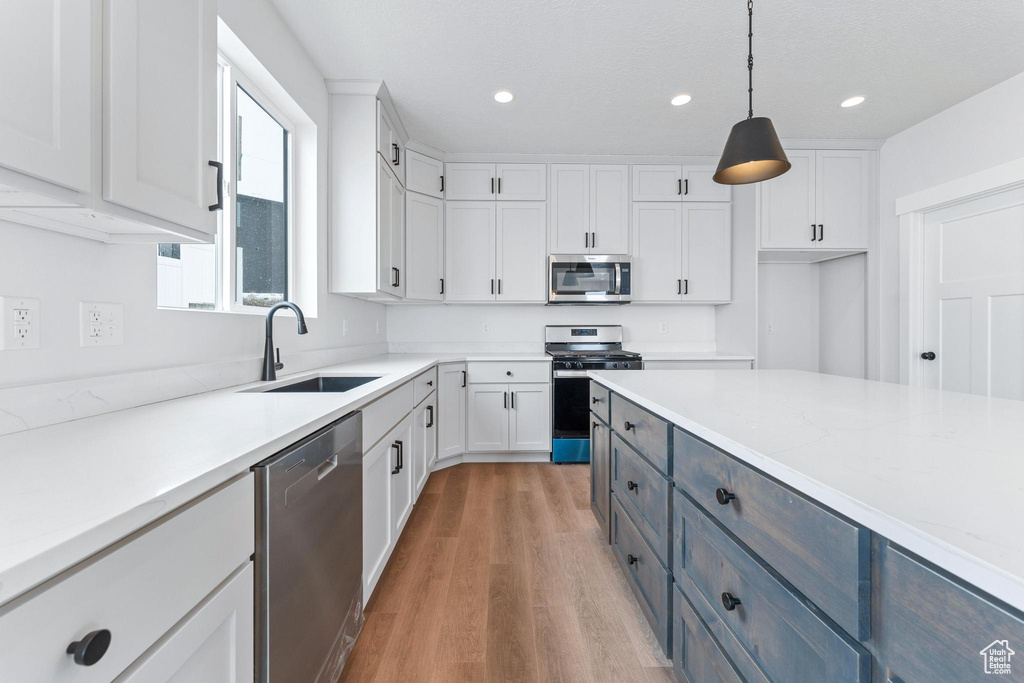 Kitchen featuring pendant lighting, light wood-type flooring, white cabinets, appliances with stainless steel finishes, and sink