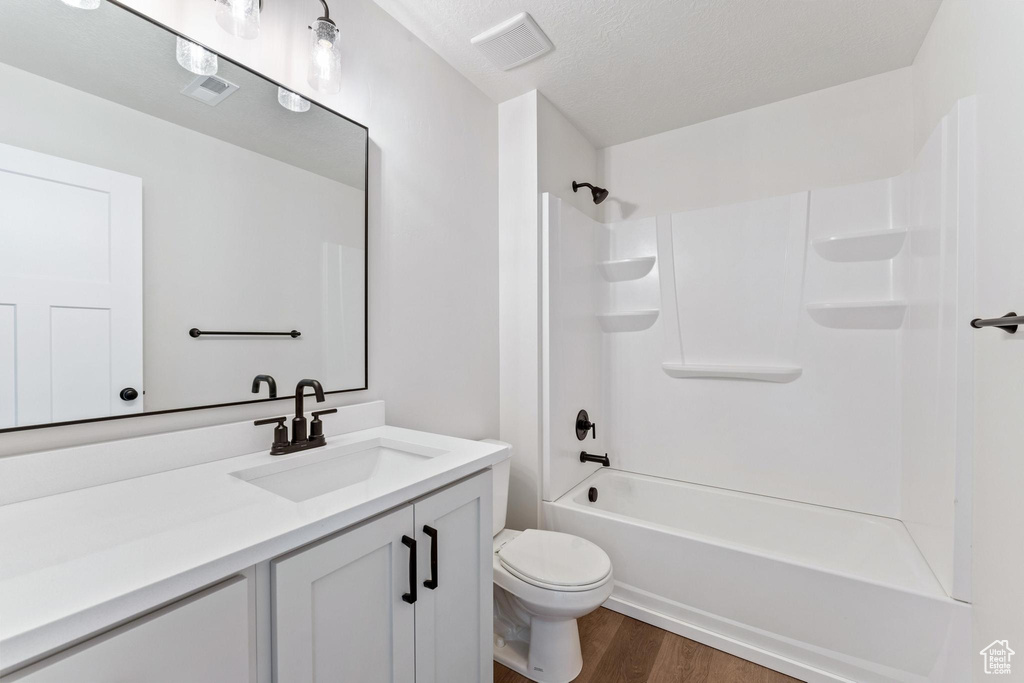 Full bathroom with hardwood / wood-style flooring, vanity, a textured ceiling, toilet, and bathtub / shower combination