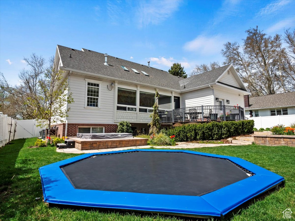 Rear view of property with a hot tub, a wooden deck, a trampoline, and a lawn