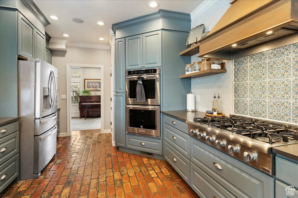 Kitchen with gray cabinets, premium range hood, backsplash, ornamental molding, and stainless steel appliances