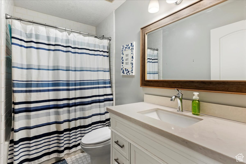 Bathroom with a textured ceiling, tile floors, toilet, and large vanity
