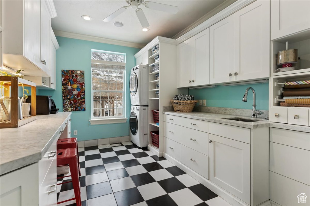 Kitchen with crown molding, white cabinetry, stacked washer and dryer, and ceiling fan