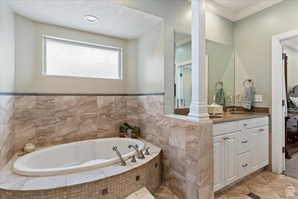 Bathroom with crown molding, vanity, tiled tub, tile floors, and decorative columns