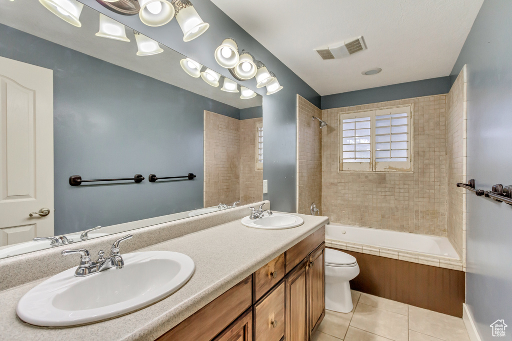 Full bathroom with toilet, dual sinks, large vanity, tile flooring, and tiled shower / bath combo
