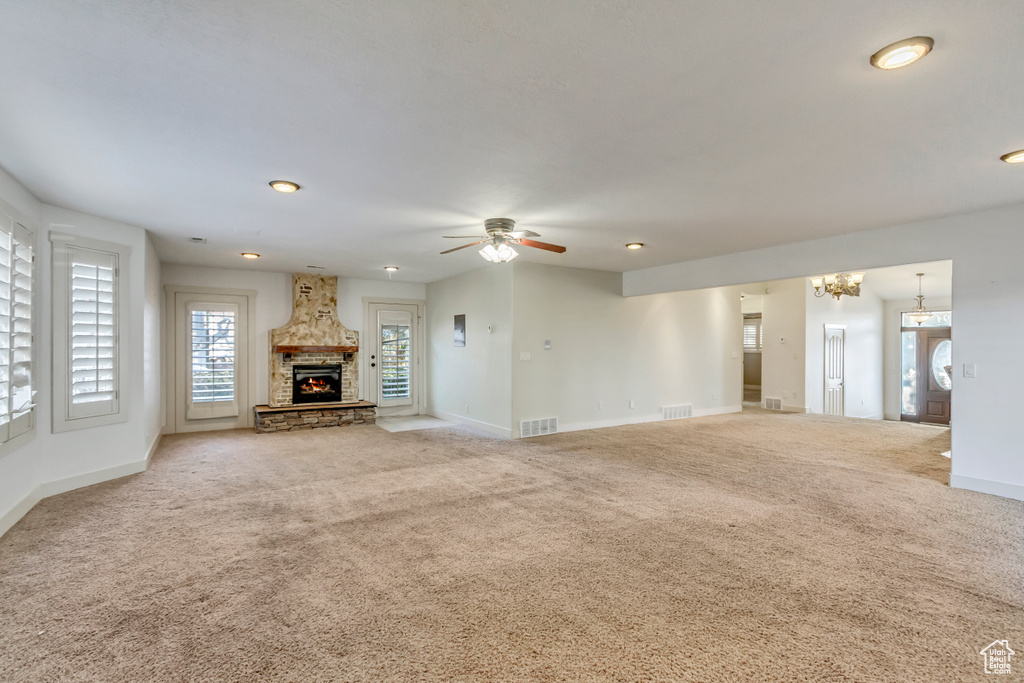 Unfurnished living room with light colored carpet, a fireplace, and ceiling fan with notable chandelier