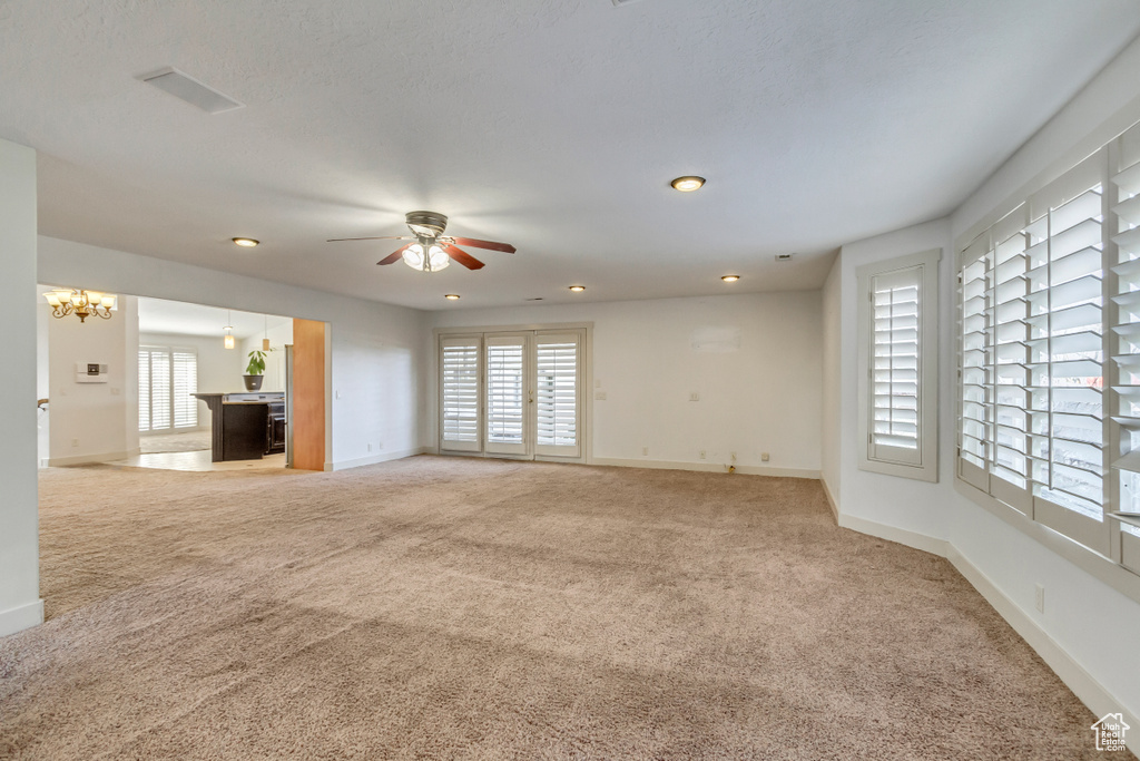 Unfurnished living room featuring light colored carpet and ceiling fan with notable chandelier